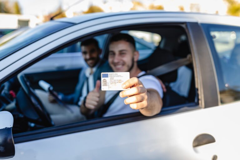 Young man successfully passed driving school test. He looking sitting in car, looking at camera and holding driving license in hand.